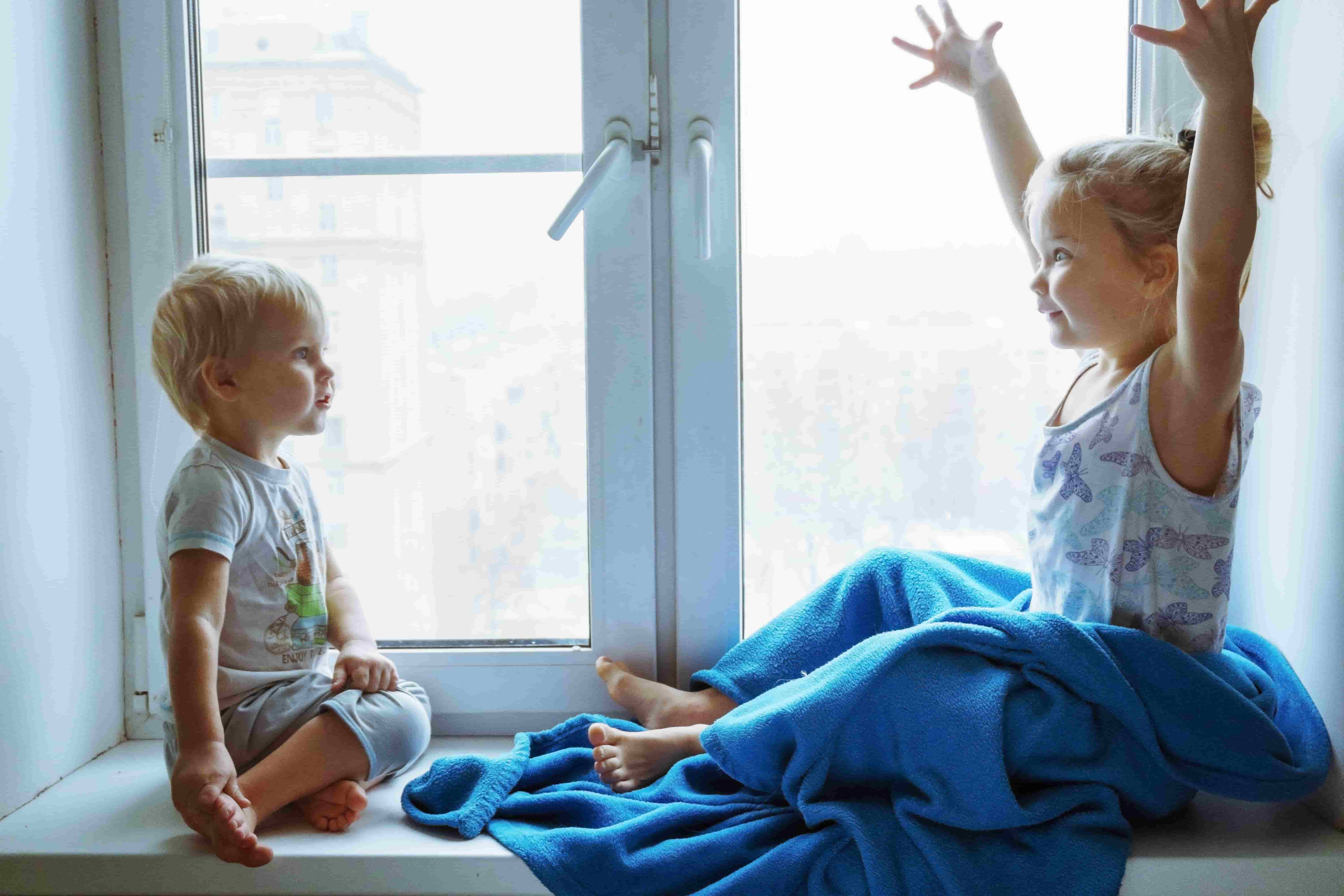 Enfants blonds face à face assis sur le rebord d'une fenêtre